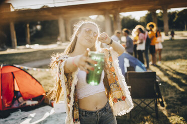 Porträt einer verspielten jungen Frau, die ein Getränk hält und auf ein Ereignis an einem sonnigen Tag zeigt - MASF12105