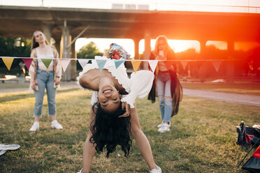 Smiling woman performing limbo dance at lawn in music festival - MASF12125