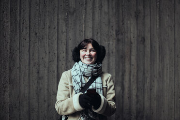 Portrait of cheerful young woman wearing warm clothing while standing against wall in subway - MASF12133