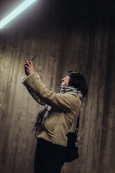 Lächelnde junge Frau, die ein Selfie mit ihrem Mobiltelefon macht, während sie in der U-Bahn an der Wand steht - MASF12134