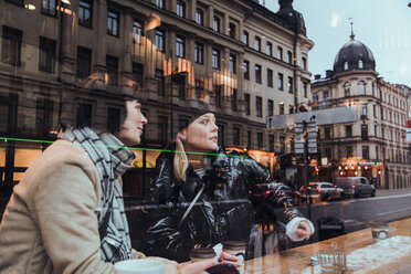 Junge Freundinnen sitzen in einem Café, gesehen durch ein Glasfenster im Winter - MASF12142