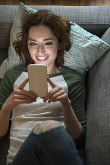 Kaukasische Frau liegt auf dem Sofa und schreibt eine SMS auf ihrem Handy - BLEF01180