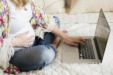 Caucasian and expectant mother using laptop on bed - BLEF01191