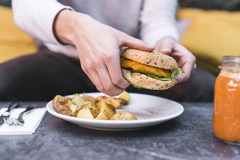 Nahaufnahme eines Mannes, der einen veganen Burger mit Kartoffeln zu Mittag isst - FBAF00448