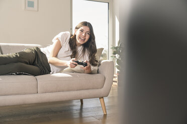 Glückliche junge Frau spielt ein Videospiel zu Hause - UUF17255