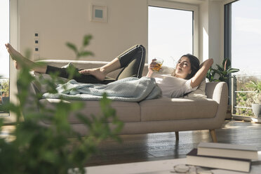 Relaxed young woman lying on couch with a drink - UUF17259