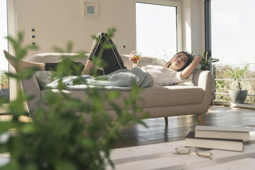 Relaxed young woman lying on couch with a drink - UUF17260