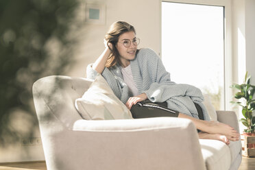 Relaxed young woman with woolen blanket on couch - UUF17261