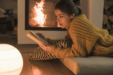 Young woman reading book at the fireplace at home - UUF17279