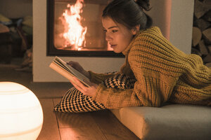 Junge Frau liest Buch am Kamin zu Hause - UUF17279