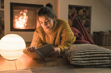 Young woman reading book at the fireplace at home - UUF17280