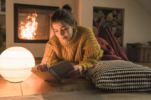 Young woman reading book at the fireplace at home - UUF17280