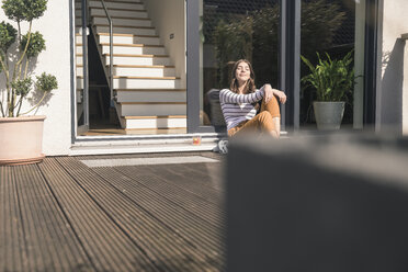 Junge Frau sitzt auf der Terrasse zu Hause und genießt die Sonne - UUF17285