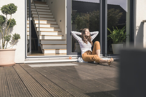 Junge Frau sitzt auf der Terrasse zu Hause und genießt die Sonne, lizenzfreies Stockfoto