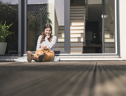 Junge Frau sitzt auf der Terrasse zu Hause - UUF17289