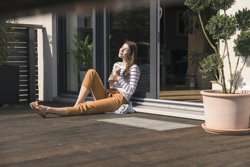 Junge Frau sitzt auf der Terrasse zu Hause und genießt die Sonne - UUF17291