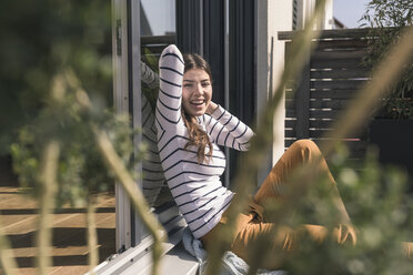 Portrait of laughing young woman sitting on terrace at home - UUF17292