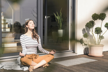 Junge Frau sitzt zu Hause auf der Terrasse und übt Yoga - UUF17297