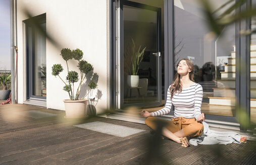 Junge Frau sitzt zu Hause auf der Terrasse und übt Yoga - UUF17298