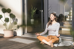 Young woman sitting on terrace at home practicing yoga - UUF17299