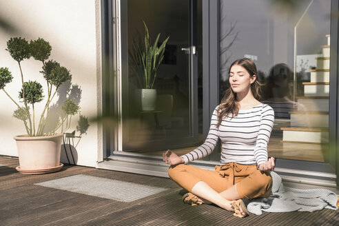 Junge Frau sitzt zu Hause auf der Terrasse und übt Yoga - UUF17299