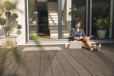 Young woman sitting on terrace at home working with book and laptop - UUF17301