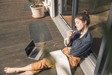 Junge Frau mit geschlossenen Augen sitzt auf der Terrasse zu Hause mit Laptop und Buch - UUF17304