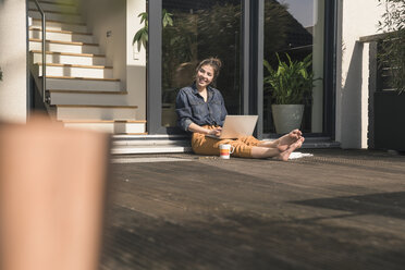 Glückliche junge Frau, die zu Hause auf der Terrasse sitzt und einen Laptop benutzt - UUF17310