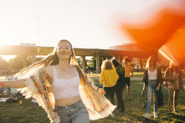 Lächelnde Frau tanzt mit Freunden im Hintergrund bei einer Veranstaltung an einem sonnigen Tag - MASF12182