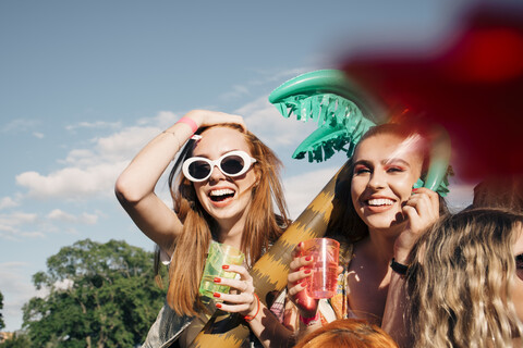 Fröhliche Freundinnen genießen Getränke bei einem Musikkonzert gegen den Himmel im Sommer, lizenzfreies Stockfoto