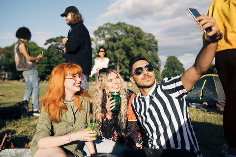 Young man taking selfie with friends on smart phone during music concert in summer stock photo