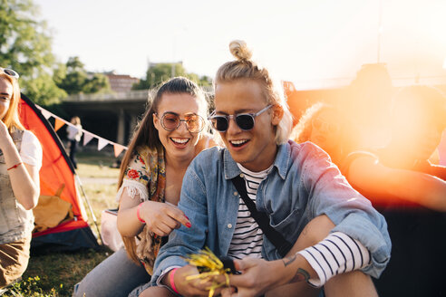 Lächelnde männliche und weibliche Freunde, die auf ihr Smartphone schauen, während sie auf dem Rasen in einem sonnigen Tag sitzen - MASF12227