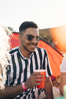 Lächelnder junger Mann mit Sonnenbrille bei einem Drink während eines Musikfestivals an einem sonnigen Tag - MASF12228