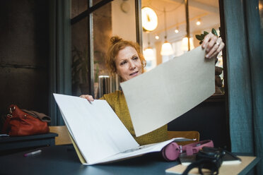 Selbstbewusste reife Illustratorin hält Papiere am Schreibtisch in einem kreativen Büro - MASF12248