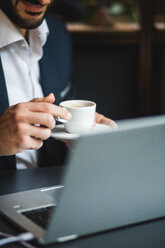 Mittelteil eines Geschäftsmannes, der Kaffee trinkt, während er einen Laptop am Schreibtisch in einem kreativen Büro benutzt - MASF12255