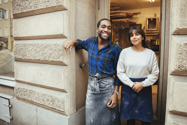 Portrait of smiling male and female artists standing at workshop doorway - MASF12263