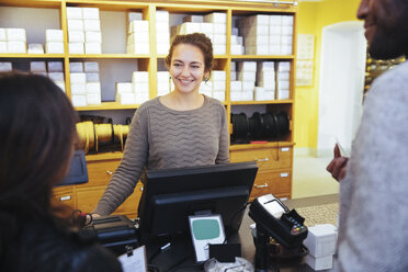 Smiling young female cashier looking at customer standing in furniture store - MASF12272