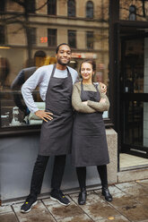 Full length portrait of confident young owners standing against delicatessen window in city - MASF12283