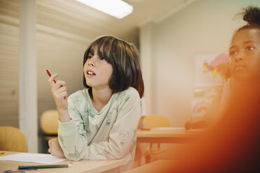 Neugieriger Junge sitzt am Schreibtisch und konzentriert sich im Klassenzimmer - MASF12292