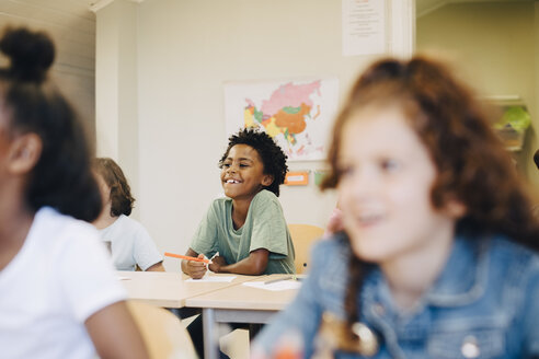Lächelnder Junge sitzt mit Freunden am Schreibtisch im Klassenzimmer - MASF12294