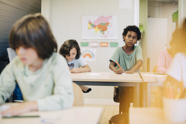 Neugieriger Junge zeichnet mit Freunden am Schreibtisch im Klassenzimmer - MASF12295