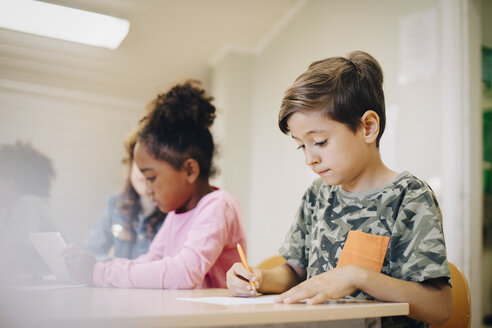Junge sitzt mit einem Freund am Schreibtisch im Klassenzimmer und schreibt auf Papier - MASF12301