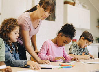 Lehrer, der männliche und weibliche Schüler am Schreibtisch im Klassenzimmer anleitet - MASF12303