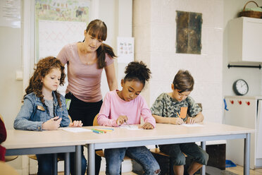 Teacher looking at students writing at desk in elementary classroom - MASF12304