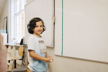 Lächelnder Junge steht am Whiteboard im Klassenzimmer - MASF12310