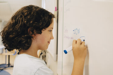 Side view of boy with curly hair writing on whiteboard at classroom - MASF12312