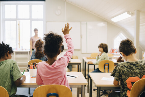 Rückansicht eines Jungen, der die Hand hebt, während er im Unterricht der Grundschule antwortet, lizenzfreies Stockfoto