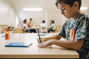 Close-up of boy concentrating while writing on paper at table - MASF12318