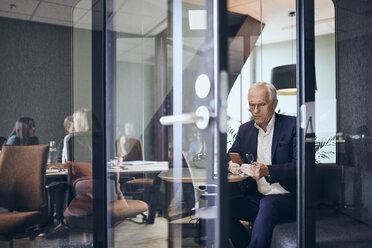 Älterer Geschäftsmann, der ein Smartphone benutzt, gesehen durch eine Glastür im Kreativbüro - MASF12340