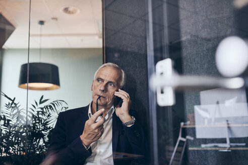 Nachdenklicher männlicher Manager, der mit seinem Smartphone telefoniert, während er sein kreatives Büro betrachtet - MASF12342